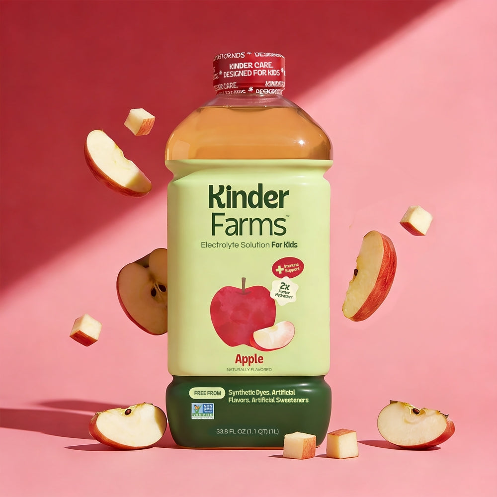 Kinder Farms Apple Electrolyte Solution bottle centered amidst floating and resting apple pieces against a pink backdrop.