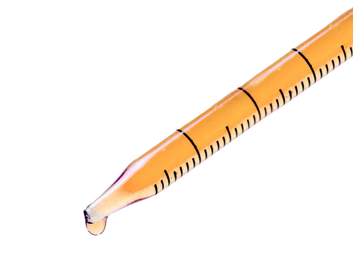 Close-up of a clear dropper filled with an amber liquid with a single drop hanging from the tip.