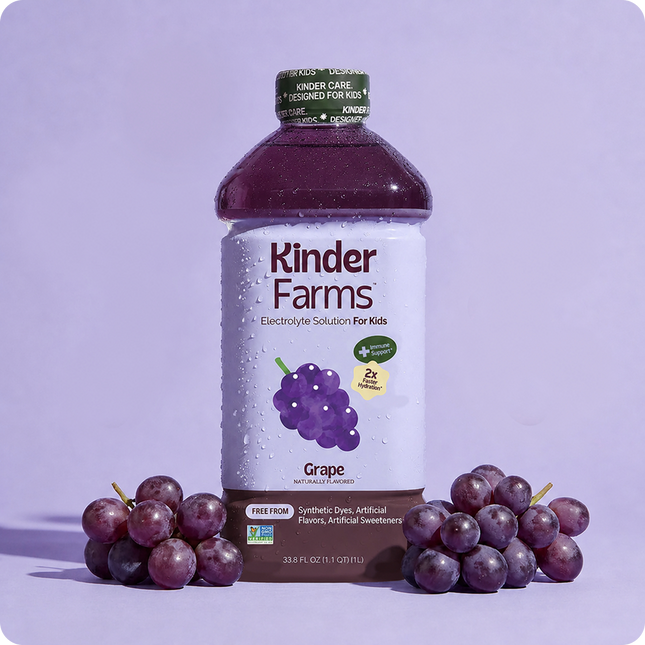 Kinder Farms Grape Electrolyte Solution bottle for kids standing between two clusters of fresh purple grapes against a light purple backdrop.