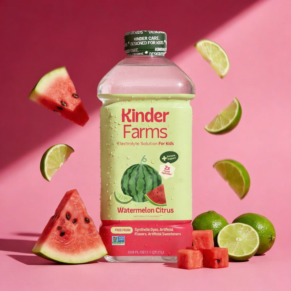 A bottle of Kinder Farms Watermelon Citrus electrolyte solution for kids, styled on a pink background with floating watermelon slices, lime wedges, and whole limes.