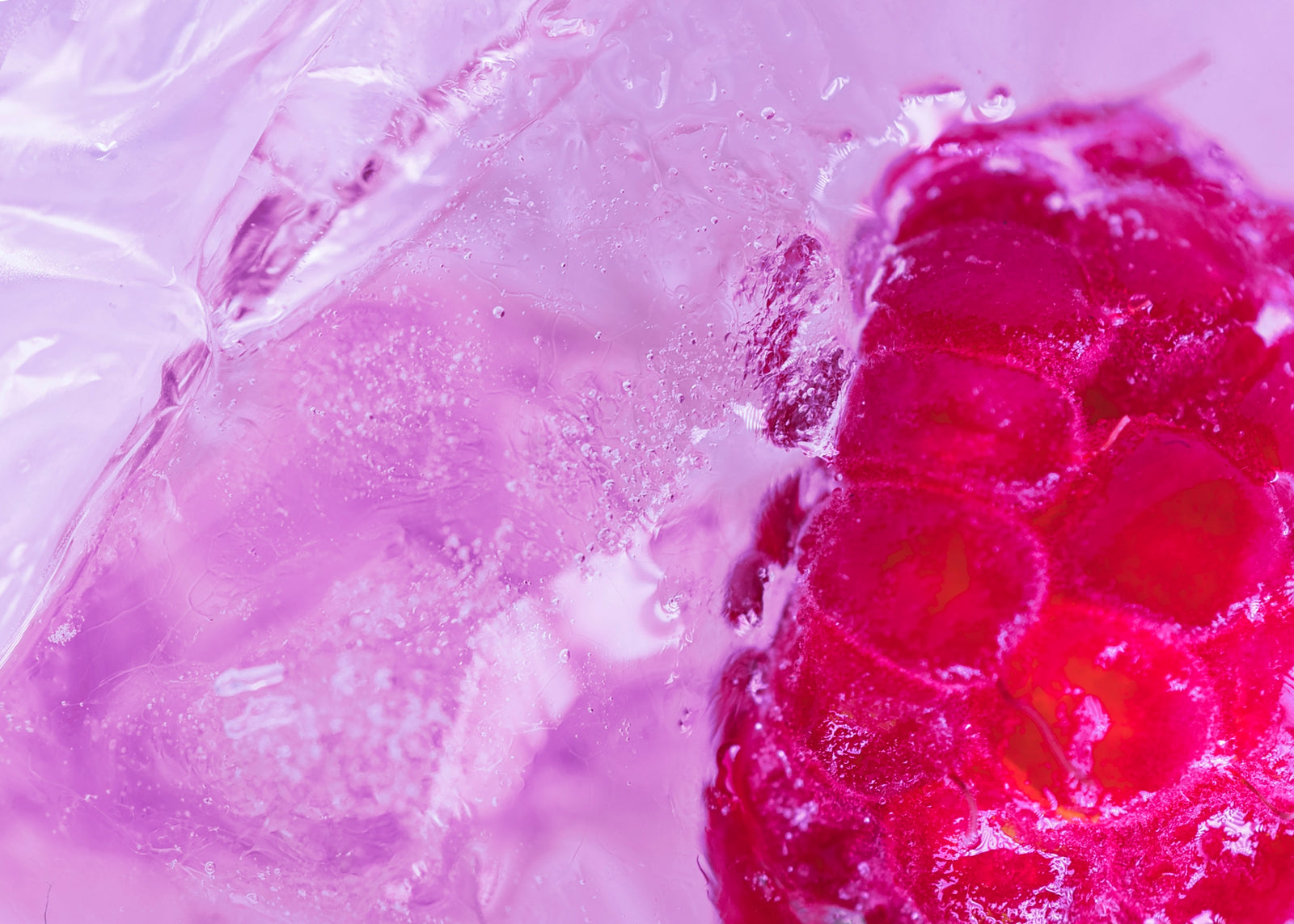 A close-up of a translucent purple liquid with ice cubes and a bright pink-red raspberry on the right side.